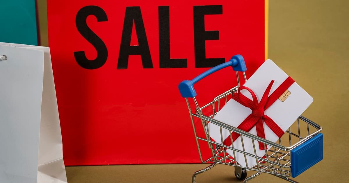 Sacolas de compras com a palavra SALE ao lado de um carrinho em miniatura