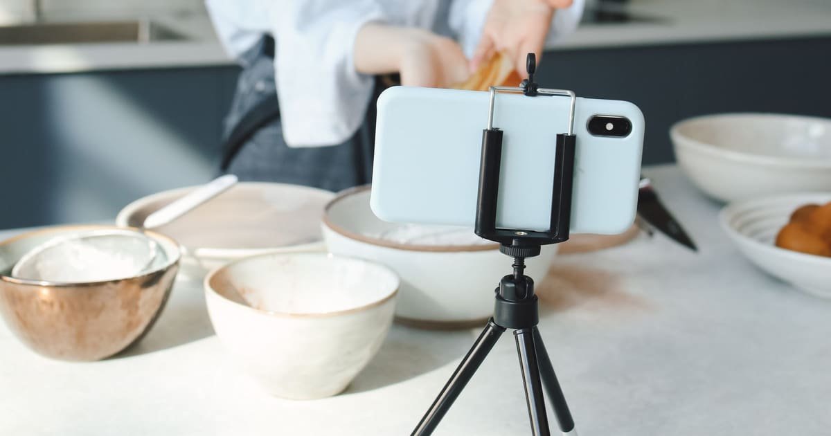 Celular no tripé gravando uma criadora preparando uma receita na cozinha