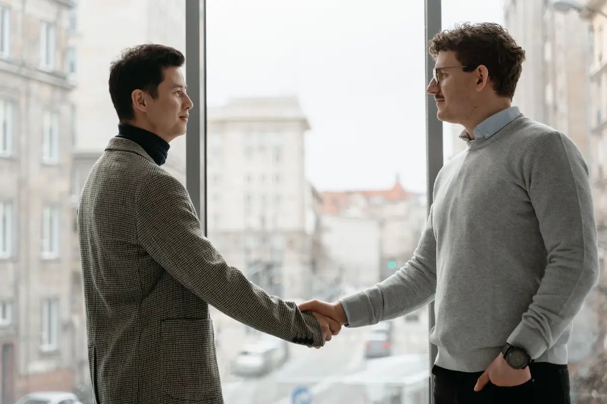 Dois homens apertando as mãos diante de uma janela de escritório