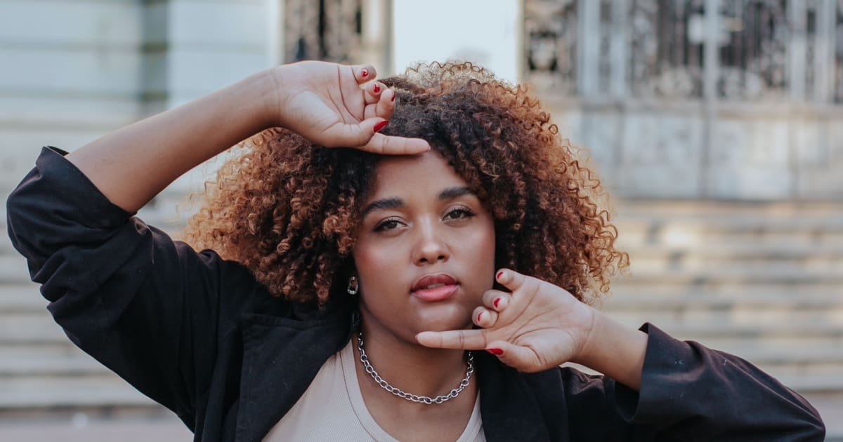 Mulher de cabelo cacheado posando diante de um prédio histórico