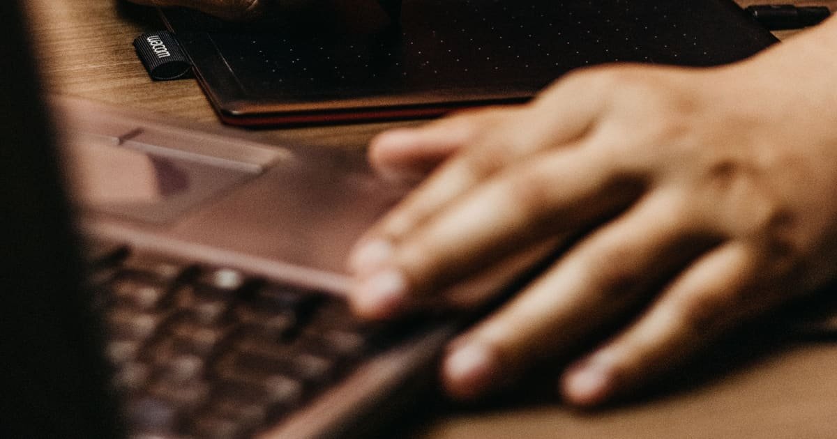Mãos escrevendo numa mesa digitalizadora ao lado do notebook