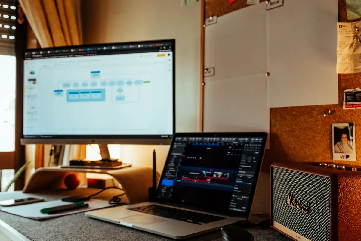 Mesa de trabalho com notebook, monitor e quadro de avisos