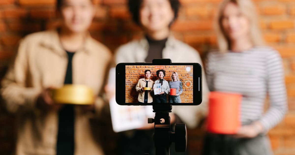 Três criadores gravando juntos com o celular no tripé, mostrando produtos para a câmera