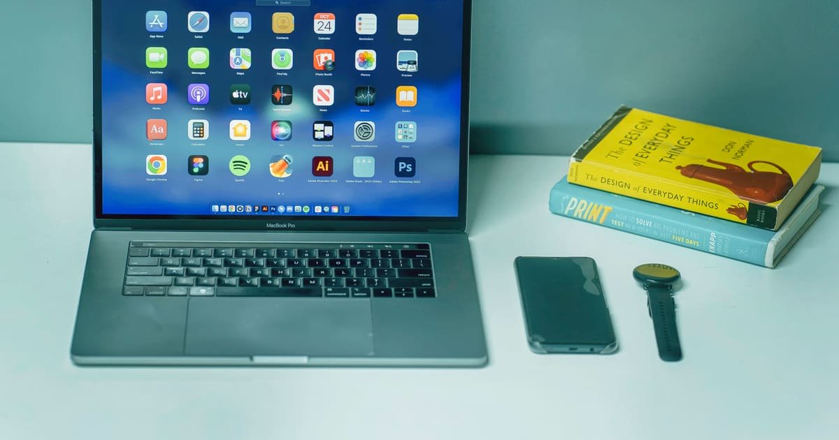 Notebook, celular e livro sobre uma mesa azul