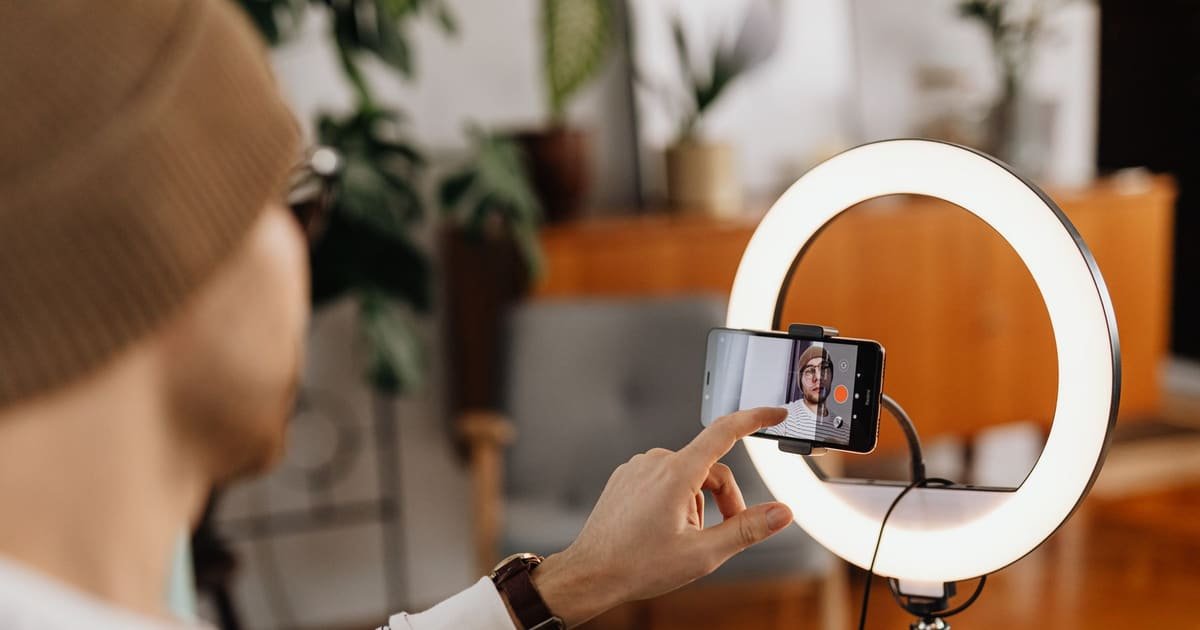 Criador ajustando o celular preso ao ring light antes de gravar em casa