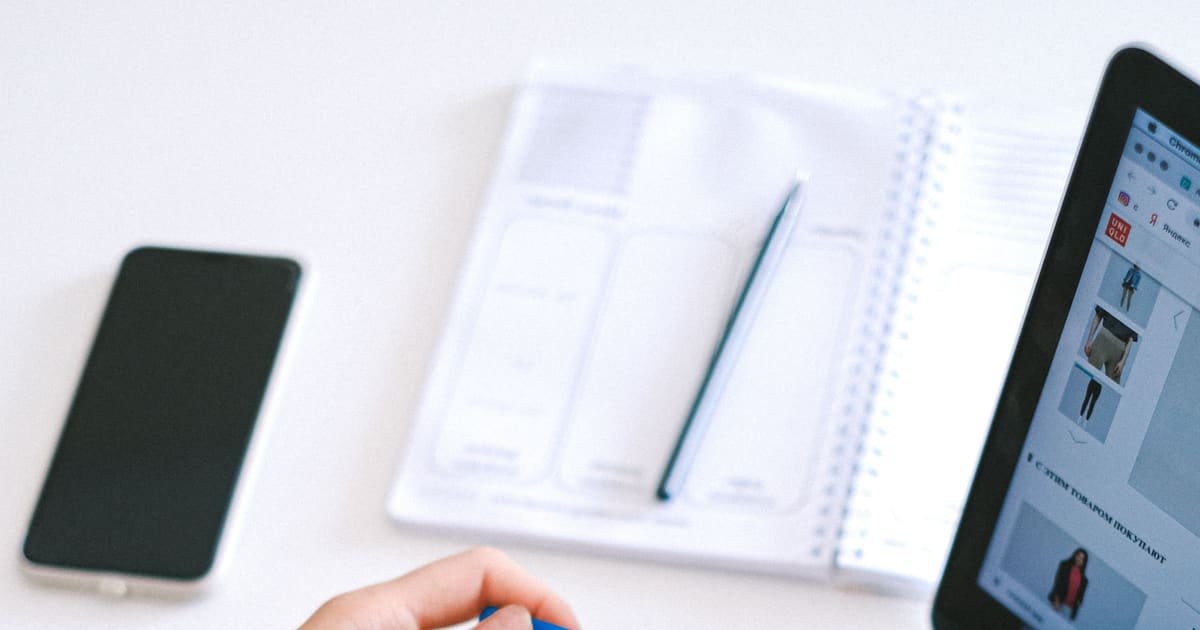 Mãos segurando um cartão diante do notebook e da agenda