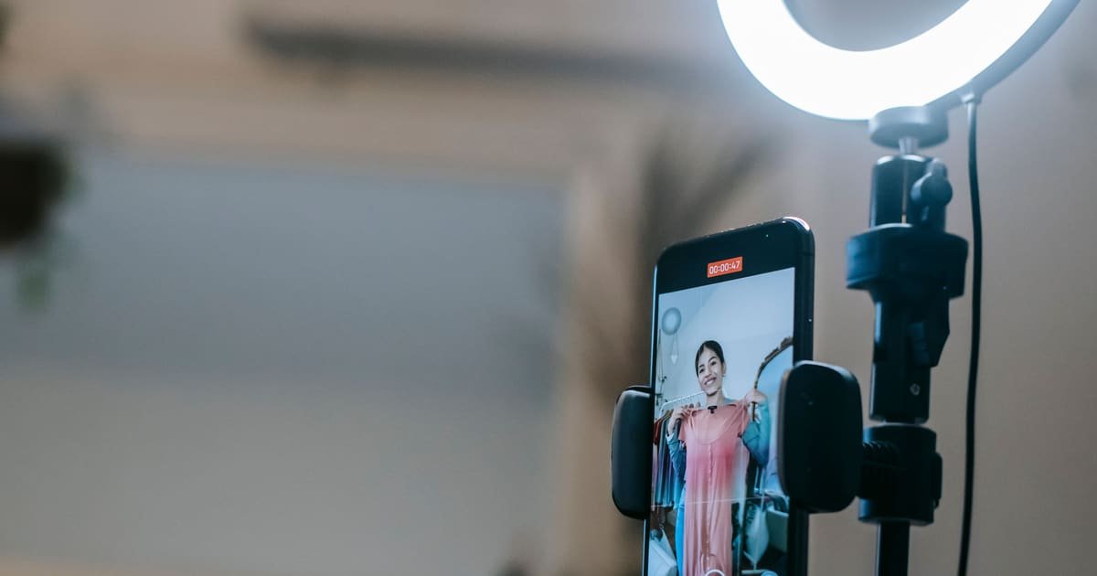 Celular preso ao tripé com ring light gravando uma criadora ao fundo